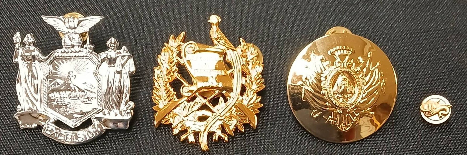 (4) Military-Style Pins and Badges: (4) Military-style pins and badges made of metal in gold-tone and silver-tone finishes. Includes detailed insignias and secure pinback closures. Marked 'N.S. Meyer Inc, New York" on one piece. In-hous