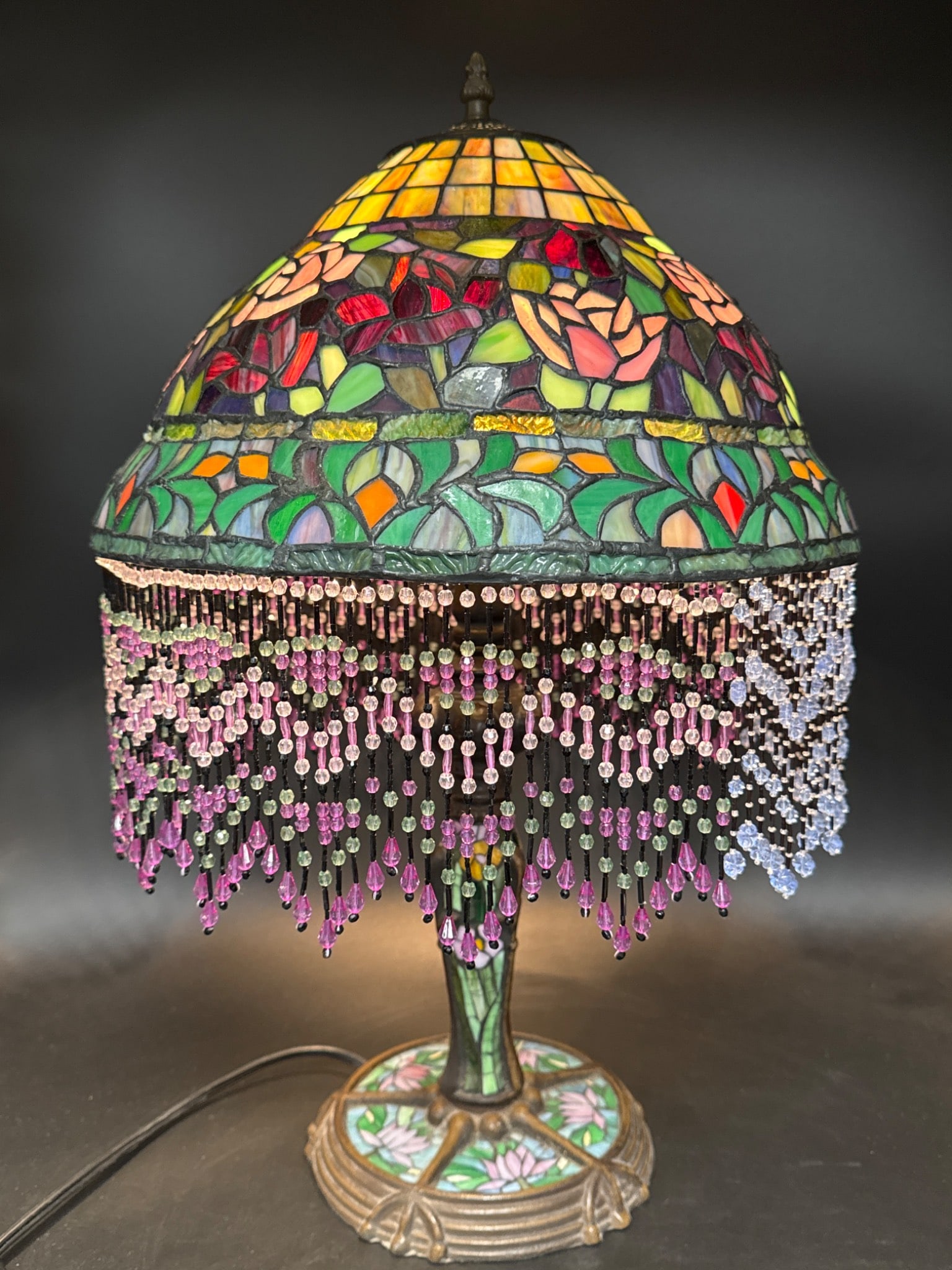 Contemporary Stained Glass Style Lamp: Contemporary lamp featuring a stained glass style design with floral motif and bead fringe, including floral embedded in base. Approx 23" tall with a 15" diameter shade. Includes electrical cord for s