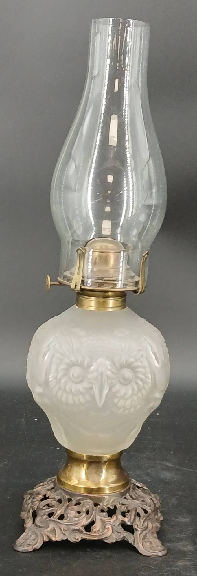 Frosted Glass Owl Head Oil Lamp: Embossed owl motif oil lamp featuring a frosted glass font and ornate metal base with clear glass chimney. Queen Anne No. 2 on brass burner. Natural wear is visible on the metal surface. Measures 10.5