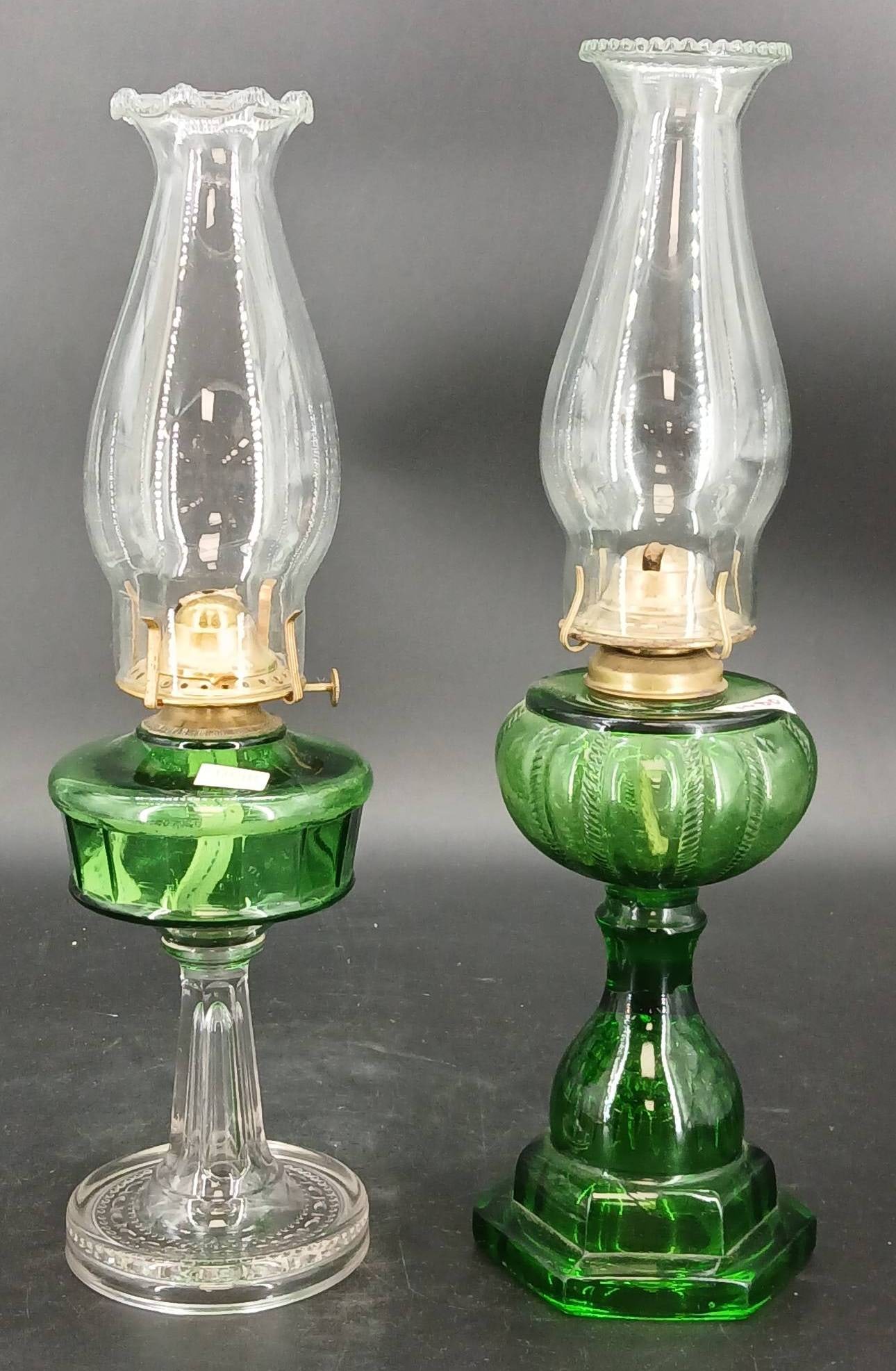 (2) EAPG Green Oil Lamps: (2) EAPG green oil lamps featuring brass burners marked 'Victor' and 'P&A Thomaston, Conn.' Includes one clear and one green base. Each lamp comes with a glass chimney. Some minor wear and chips noted