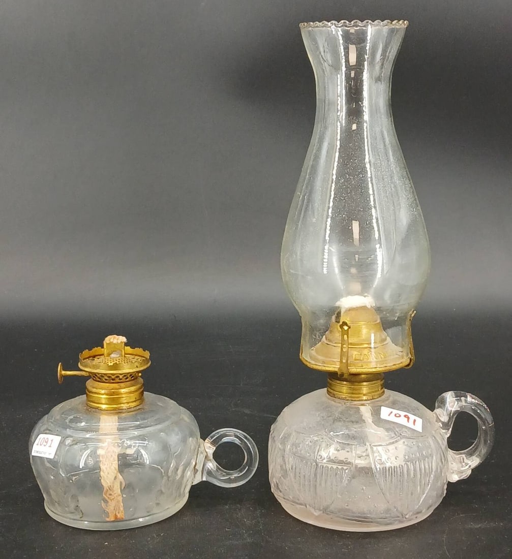 (2) EAPG Finger-hold Oil Lamps: (2) EAPG finger-hold oil lamps featuring decorative patterns and brass burners. One features pressed leaf design and other features flag emblems. Both lamps show minor wear consistent with prior use. 