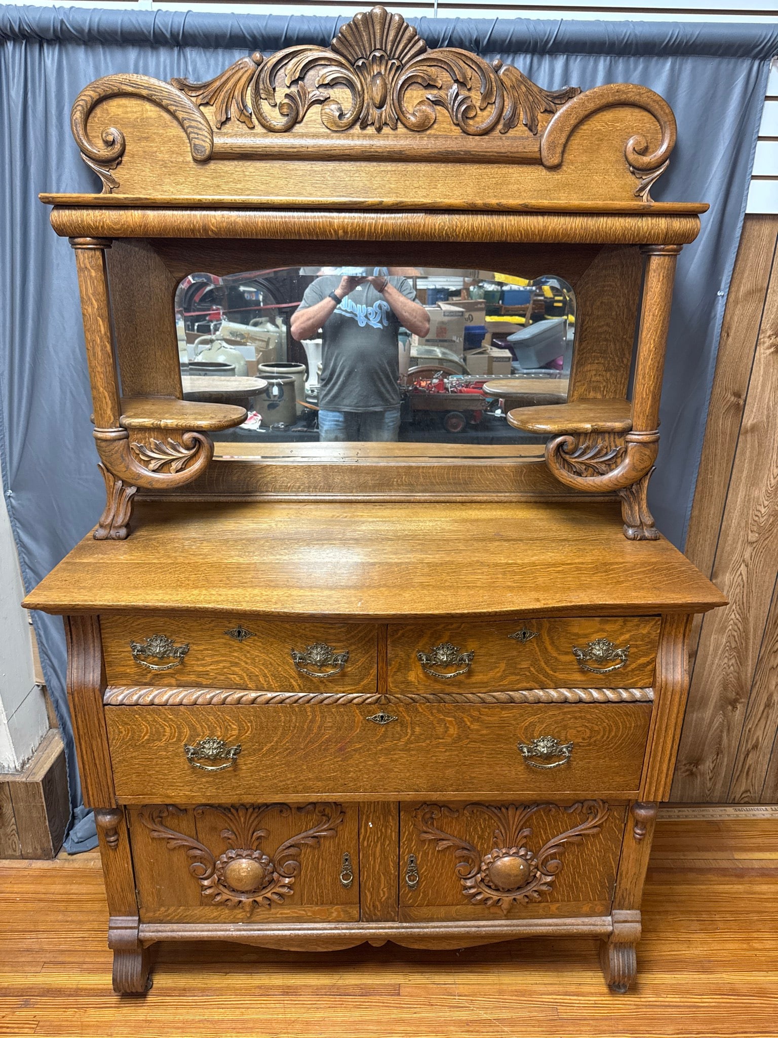 Carved Oak Hooded Sideboard With Mirror: Ornate oak hooded sideboard featuring detailed carved decoration, a large beveled mirror, brass hardware, and two knick-knack shelves. Two drawers and lower swing out doors storate. Measures 80" tall,