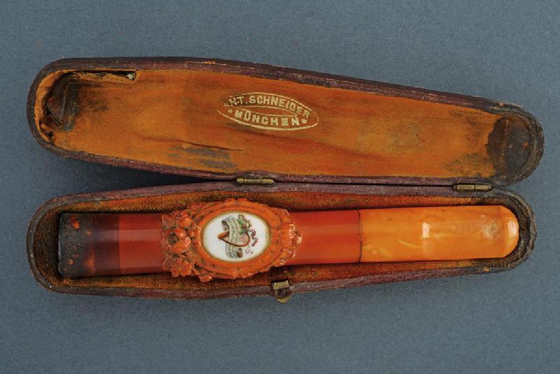 A cased cigar holder: dating: provenance: Munich, In amber, central part embossed with floral motifs and with oval, porcelain, hand-painted plate. In original case marked 'ANT. SCHNEIDER MÃœNCHEN'. On the cover written i