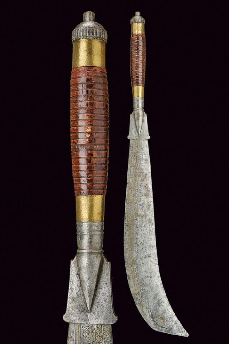 A ram dao: dating: 19th Century provenance: Nepal, Heavy, big, single-edged blade engraved with geometrical motifs and an eye, partially inlaid with brass. Twisted, wooden grip with iron and brass mounts. length