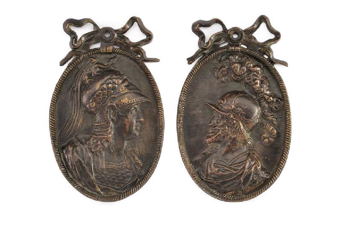 A lot of two bronze plaques: dating: 18th Century provenance: France, Of oval shape, decorated with a tuft, portraying two antique warriors with armor and plumed helmet in relief. dimensions 9.1 - 14.2 cm.