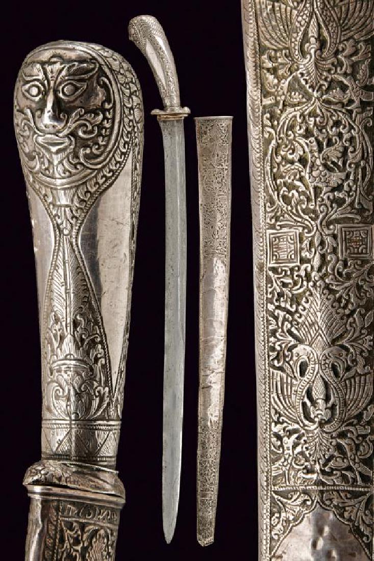 A silver mounted parang: dating: Late 19th Century provenance: Indonesia, Strong, single-and false-edged blade, in fine pamor, with groove on the back; grip and scabbard covered with silver foil, embossed and engraved with bi