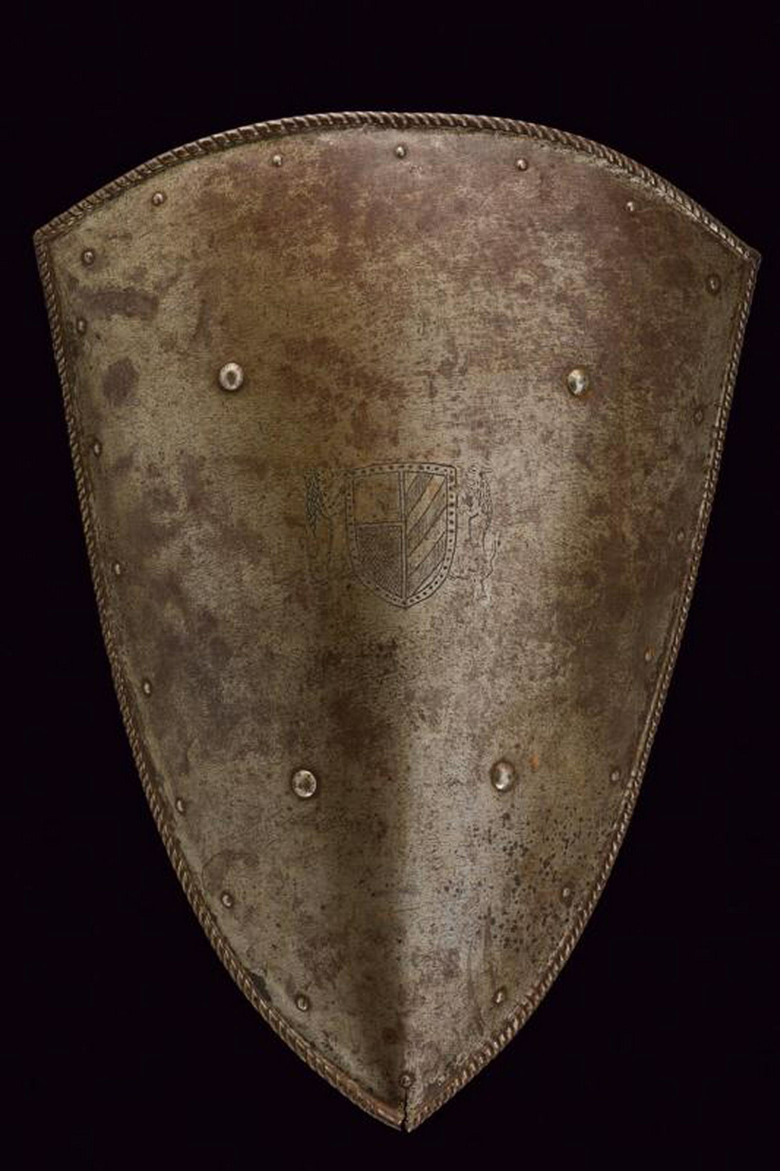 A shield with heraldic emblem: dating: 19th Century provenance: Europe, In iron, of convex shape. With engraved heraldic emblem in the center. File-roped and twisted borders. Back without enarmes. Four, central studs and a row of r