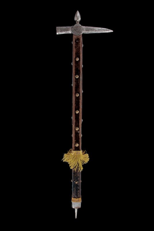A war-hammer: dating: late 16th Century provenence: Eastern Europe Octagonal beak with a simple weavy design, ringed hammer, with semicircular wings, pinecone-faceted cusp, flat straps; wooden shaft covered with ve