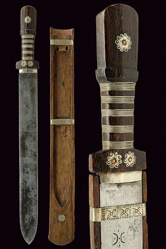 A short sword: dating: 19th Century provenance: Bhutan Strong and heavy, single-edged blade with a mark at the forte; wooden grip decorated with silver bands and rosettes; complete with wooden scabbard with silver m