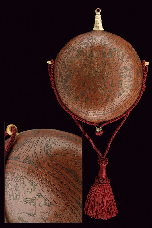 A powder-flask: dating: 19th Century provenance: Italy Oval body made of a pumpkin, finely engraved with effigy of human figures and floral motifs. Fuse with stopper and bone suspension rings. dimensions: height 22 c
