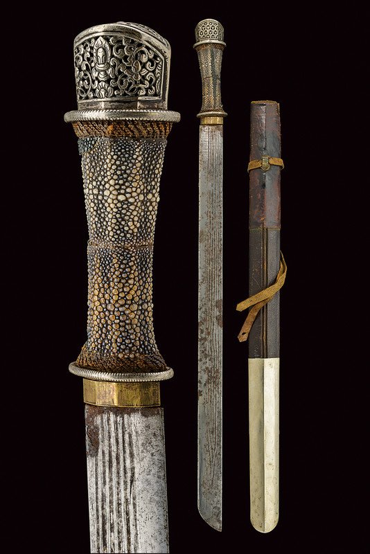 A patag (sword): dating: 19th Century provenance: Bhutan Heavy, straight, single-edged blade with grooves; wooden grip with ray-skin covering and silver hilts, the pommel richly pierced and engraved; wooden scabbard w