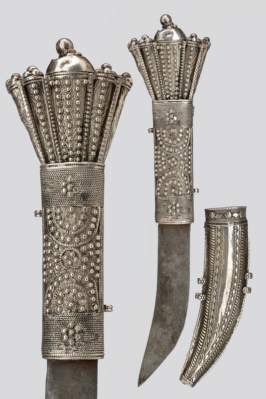 A Shafra (knife): dating: circa 1900 provenance: Arabia Simple, curved, , slightly engraved, single-edged blade; silver-inlaid mounts and scabbard, richly decorated with filigree and engravings. These knifes used to be