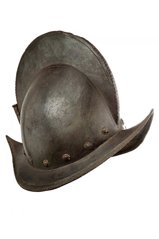A morion: dating: 16th Century provenance: Europe Iron skull in one piece, surmounted by a relieved crest with twisted border. A row of rivets with brass rosette (a pair of substitutions) at the base of the sku