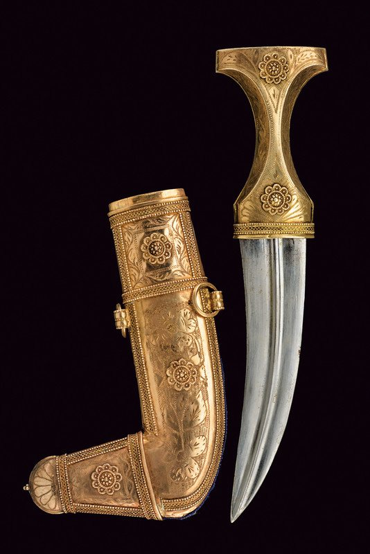 A jambiya: dating: 20th Century provenance: Arabian Peninsula Curved, double-edged blade with raiser at the center. Gilt, silver grip engraved with racemes and two, relieved rosettes. Scabbard decorated en suite