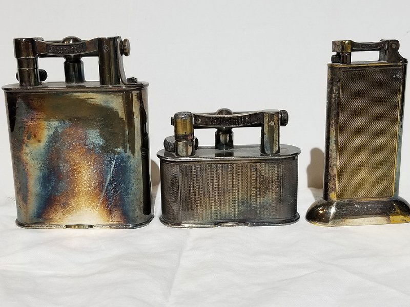 Three Dunhill lighters: Three Dunhill table lighters, from the Estate of Anne Rubin Klein, NYC.These lighters are very tarnished but can be polished. Largest lighter: 4" high.