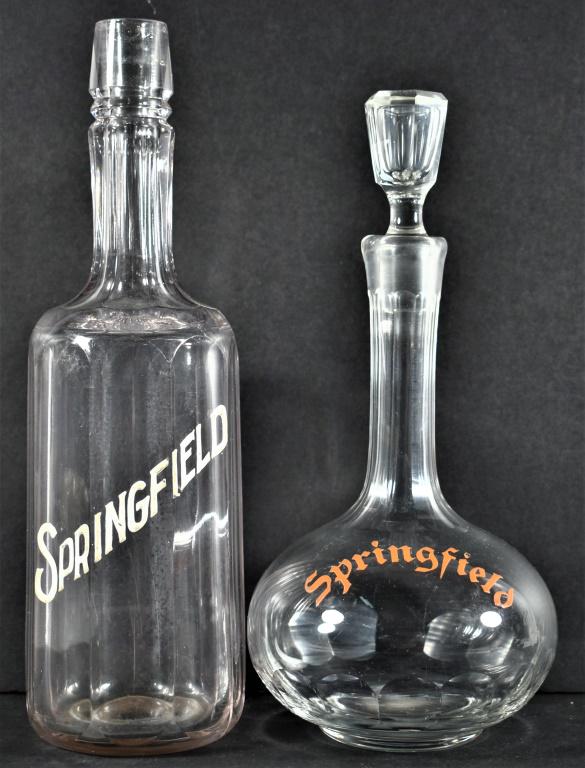 Two Enamel Label Springfield Whiskey Bottles: Two Enamel Label Springfield Whiskey Bottles. Decanter with red lettering, ground glass stopper, no chips or cracks, 10 1/2 inches overall. Back bar bottle has stopper crescent crack at top, 11 1/2 in