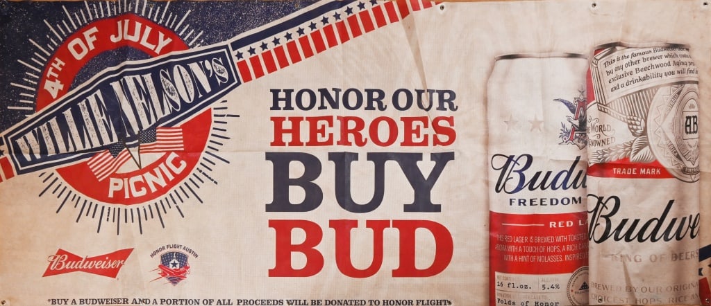 Willie Nelson 4th of July Picnic Banner: Willie Nelson 4th of July Picnic banner with slogan, "Honor Our Heroes, Buy Bud" sponsored by Budweiser. In 2018 Budweiser released Budweiser Freedom Reserve Red Lager. 4ft x 10ft