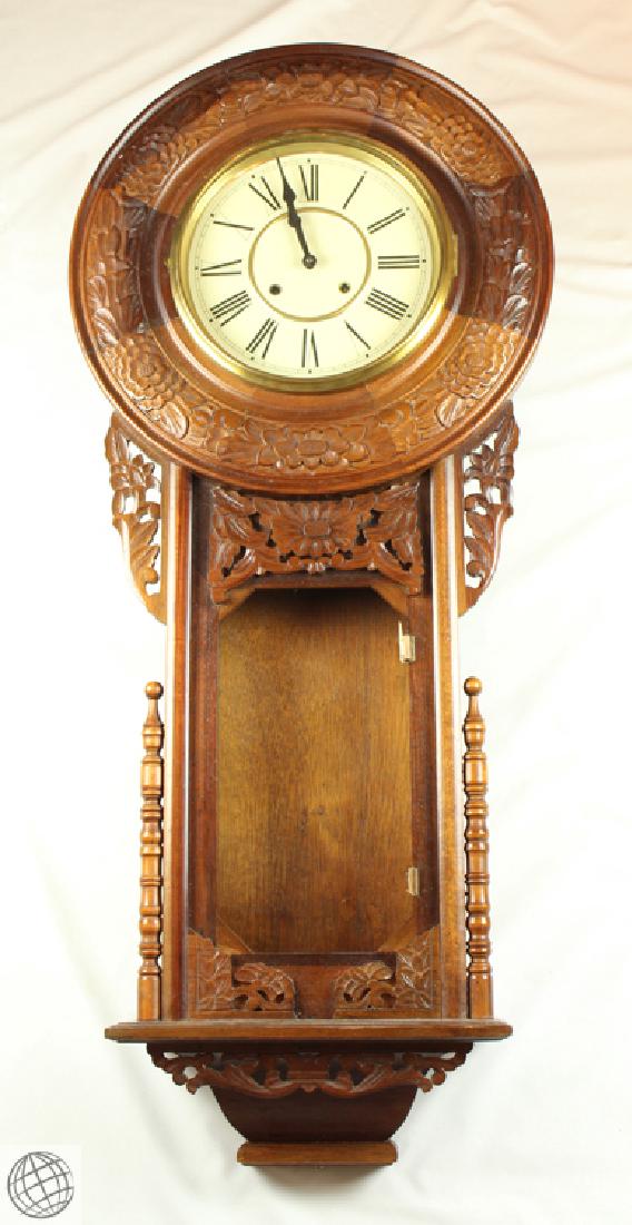 Decorative CARVED CABINET LARGE WALL CLOCK Brass: Details: Large decoratively carved wall clock. Measures approx. 56" tall by 5 1/2" deep by 22 1/4" wide. Brass pendulum, and brass accented glass door over face. Black Roman numerals and hands, on wh