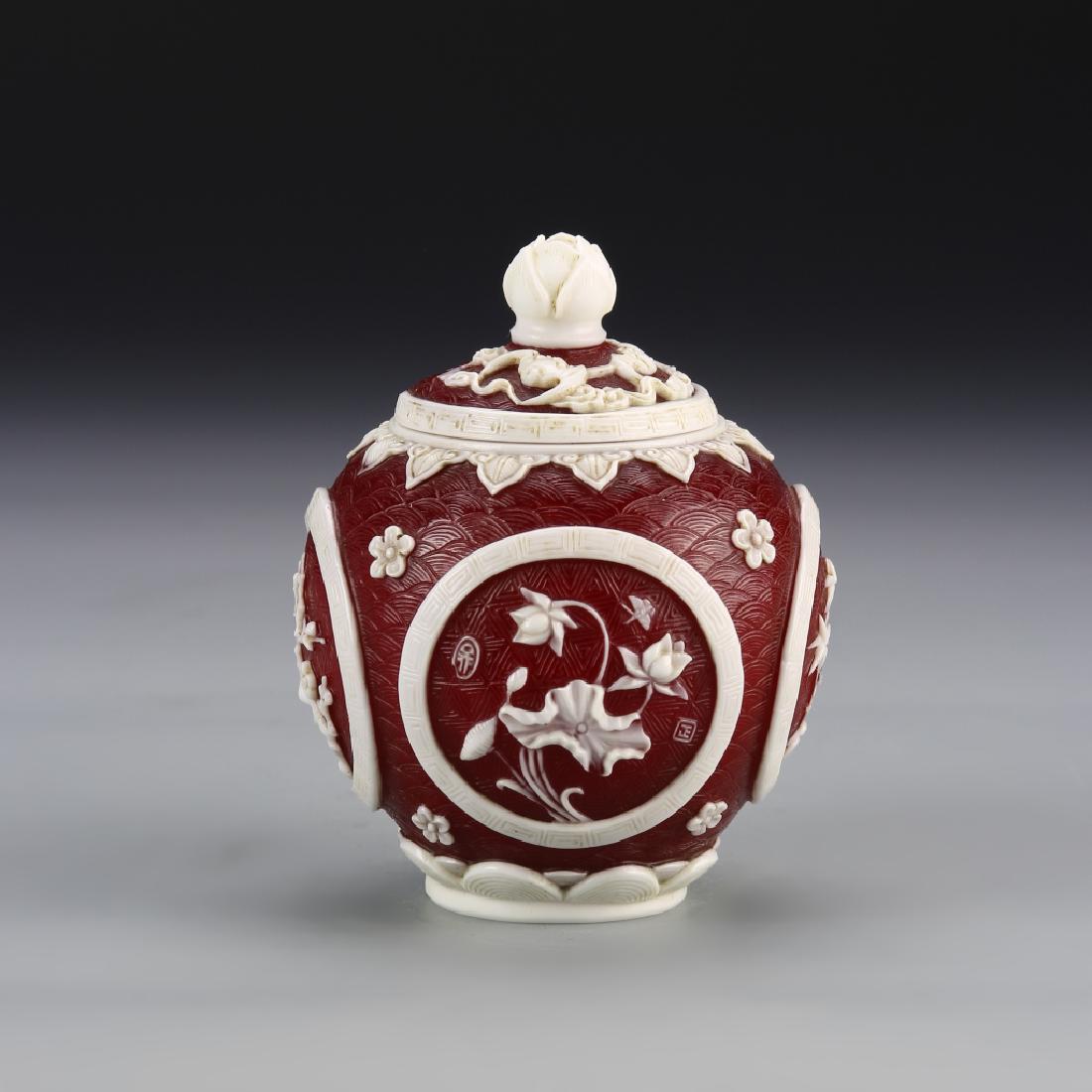 Chinese Peking Glass Jar: China, Peking glass jar, in a deep red hue, with raised relief details in white glass, and carved linear patterns across the surface, with cover, mark on base. Height 4 1/2 in.