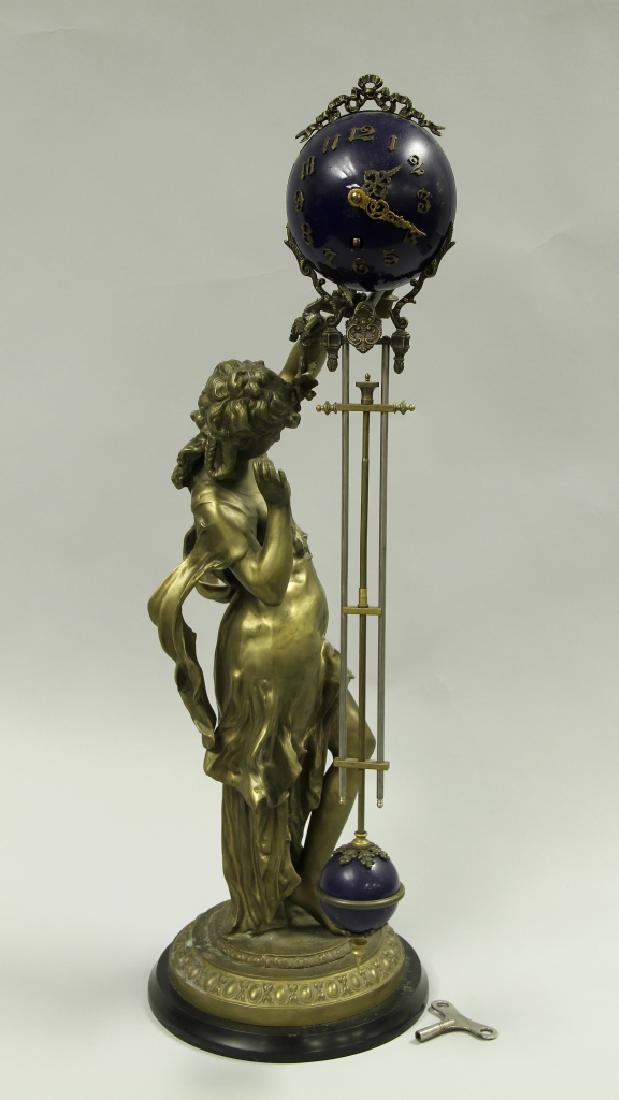 French Mystery Clock: France, a mystery clock, the clock face a bright blue colors with Arabic numerals and minute and hour hands, leading down and terminating in a smaller blue pendulum, all held by the bronze sculpture o