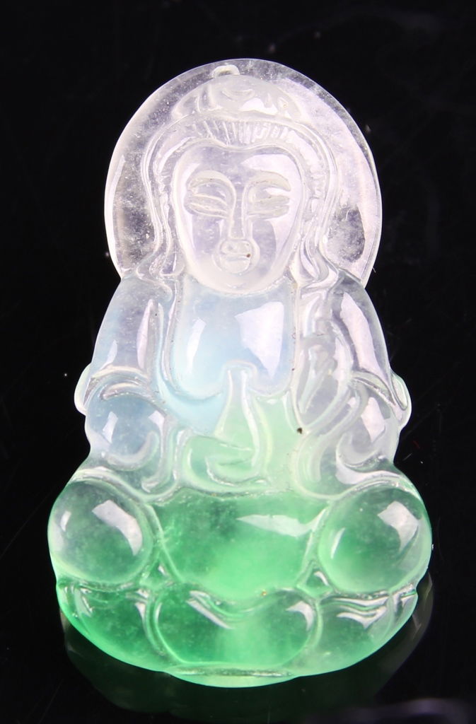 Chinese Jadeite Guanyin Pendant: China, jadeite Guanyin pendant, polished surface, seated figure, in a flowing robe, deep green visible in base, fading to a translucent hue. Height 1 1/4 in.