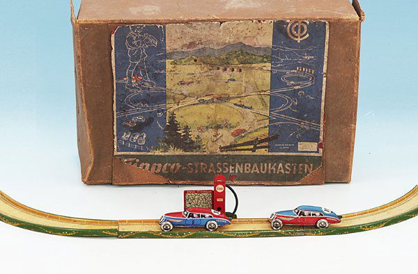 Konvolut TippCo Reichsautobahn-Teile: Fahrbahnstücke, Weichen, Tankstelle, zwei Uhrwerkautos, mit mehr oder weniger deutlichen Gebrauchsspuren, im nicht zugehörigen Karton auf dem ein Teil des Originalkartons aufgeklebt wurde