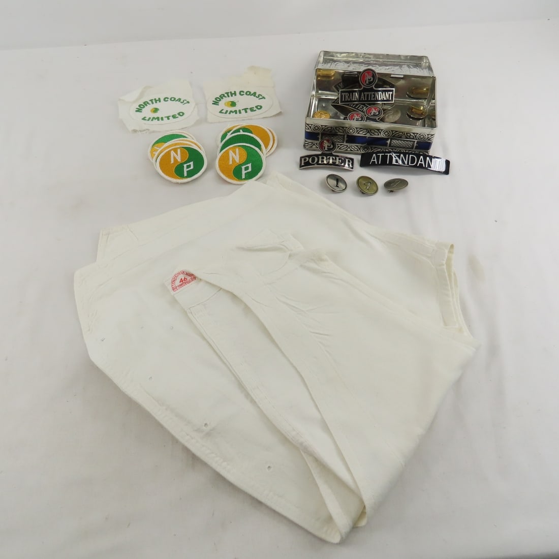 Northern Pacific Badges, Waiters Numbers & More: Waiters vest (not marked), 9 metal number badges, 1 metal porter hat badge, 5 attendant hat badges ( 4 metal & 1 unmarked plastic),3 button covers, and patches. From the Collection of Don L. Hofsomer.