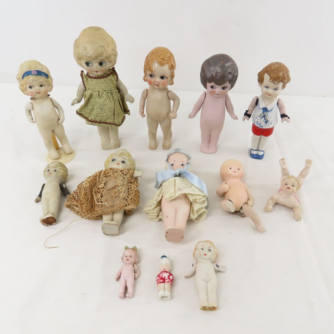13 German & Japan Kewpie Bisque Dolls: 13 German & Japan Kewpie Bisque Dolls - 6" doll in red shorts is marked:152 SSK 14 Germany, Dark hair Kewpie & 2" with green bow are Germany, smallest & lace with blue bow are unmarked, all others