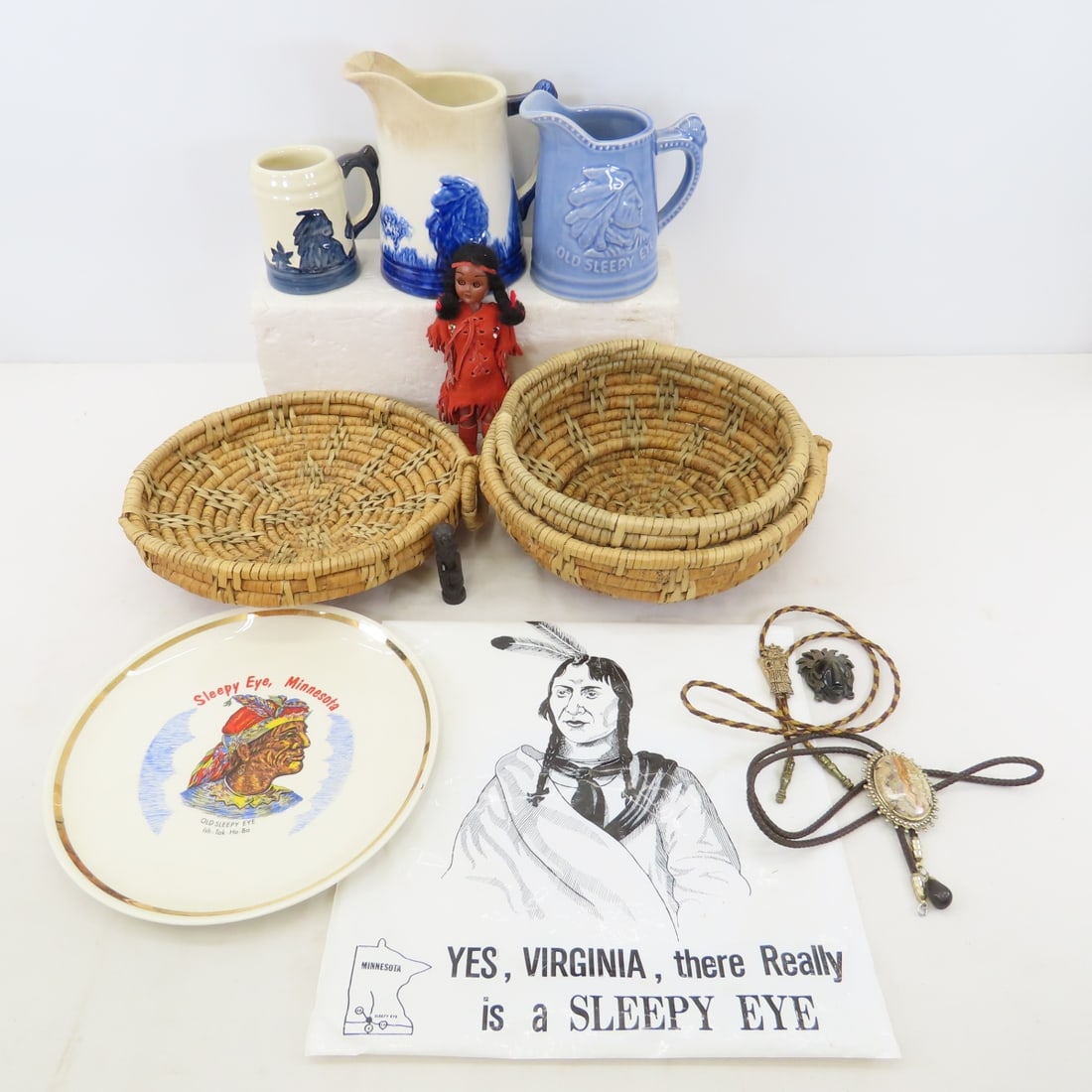 Sleepy Eye Plate, Pitcher, Basket & Bolo Ties: Sleepy Eye Plate, Pitcher, Basket & Bolo Ties - Sleepy Eye Stoneware Pitcher- heavy crazing, Sleepy Eye Convention Pitcher, Mug & Plate. Wicker Basket, Skookum Doll & Bolo Ties. Lot Size: 14 x 12