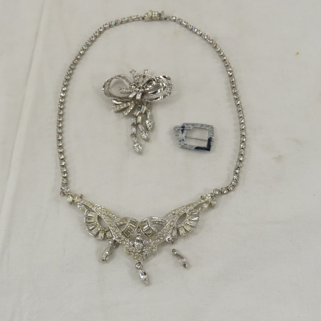 2 Sterling Silver Rhinestone Brooches & 1 Necklace: 2 Sterling Silver Rhinestone Brooches & 1 Necklace - 1) signed sterling bow and rhinestone brooch- no missing stones (signature is a shield with a W?) 11grams, 2) small square brooch marked