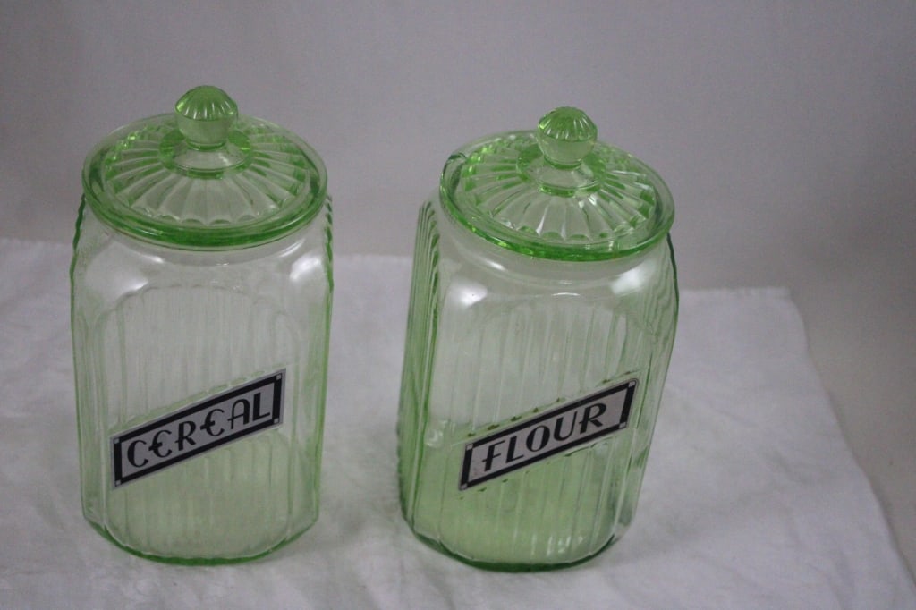 2 Green Uranium Glass Ribbed Canisters -Glows: 2 Green Uranium Glass Ribbed Canisters -Glows - 2 Anchor Hocking Green Uranium Glass Ribbed Canisters. Cereal and Flour 9" Tall. Cereal has Rim Chips and Lid Rim Chips. Lot Size 10" x 8" x