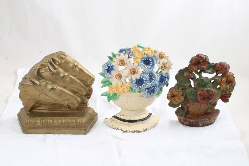 3 Cast Iron Door Stops: 3 Cast Iron Door Stops - Triple Horse Heads, 7" Flower Pot, 8" Flower Pot Cast Iron Door stops. Lot Size 8" x 8" x 8". 15 Lbs. Photos are part of description (Live Auctioneers on displays a max