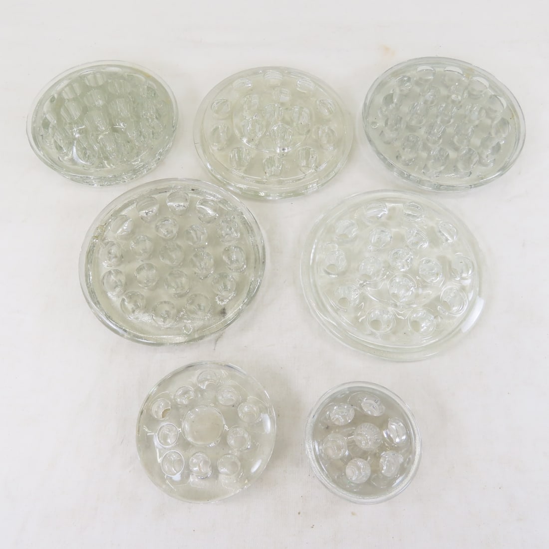 7 Antique Glass Flower Frogs: 7 Antique Glass Flower Frogs - largest is 5" across. LOT SIZE: 12x7x6", 6 LBS All information and photos are intended to be as accurate as possible, but errors are possible. No item may be returned