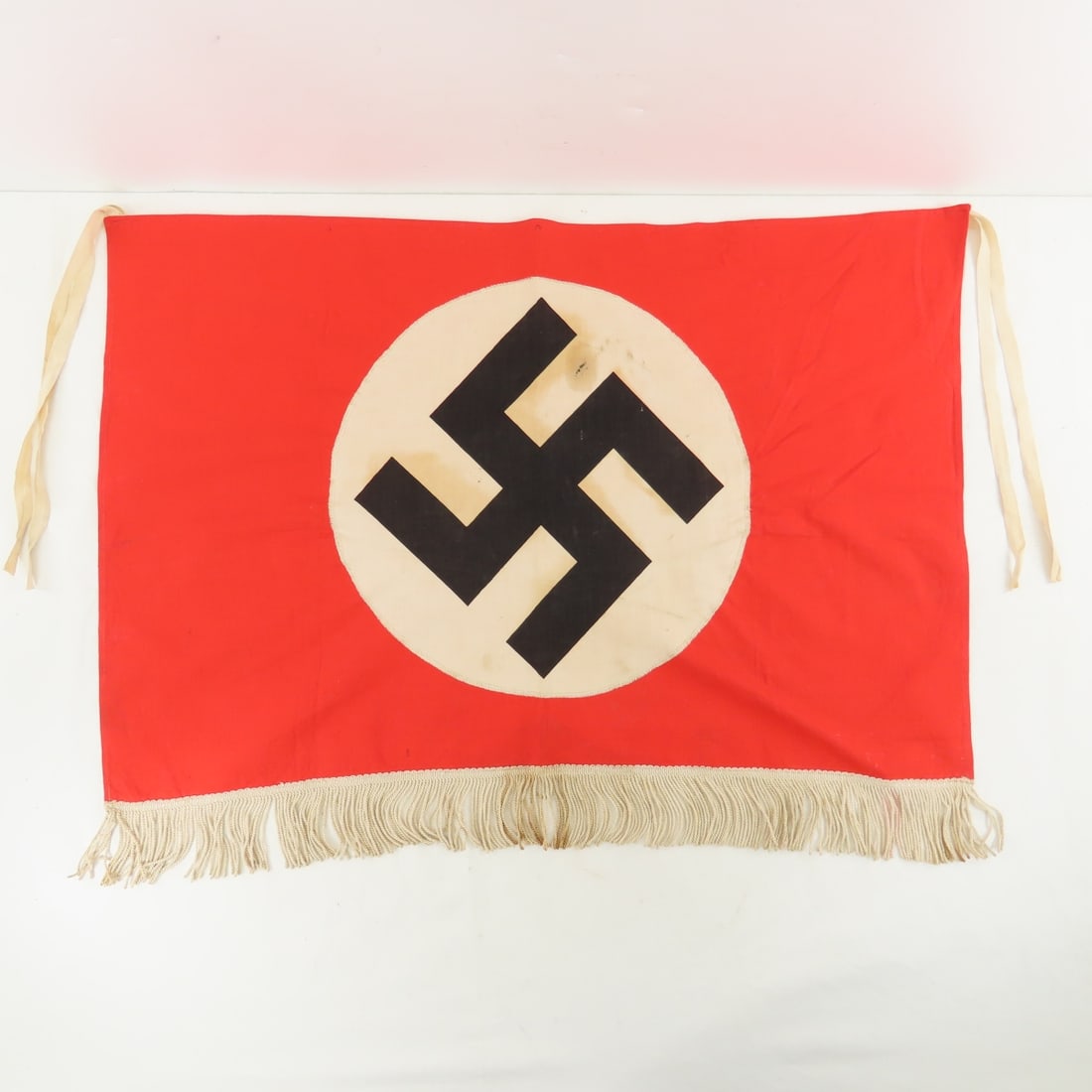 WWII German Swastika Flag with Ties & Fringe: WWII German Swastika Flag with Ties & Fringe - Some stains, printed swastika on white circle sewn onto flag, cloth ties. measures @ 27x22". LOT SIZE: 8x6x2" 1 LB All information and photos, which are