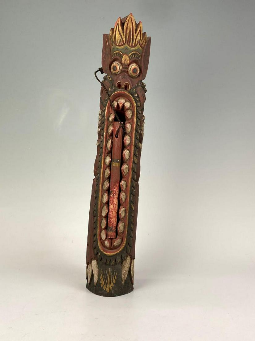 Indonesian Polychrome Wooden Percussion Instrument: Hand Carved Tribal Instrument, Painted Colors of Red, Gold, Green, White, and black. Played by taking attached stitch and rubbing against teeth. Approximately 4" x 4.5" x 23.8125" with a stick 9.75" x