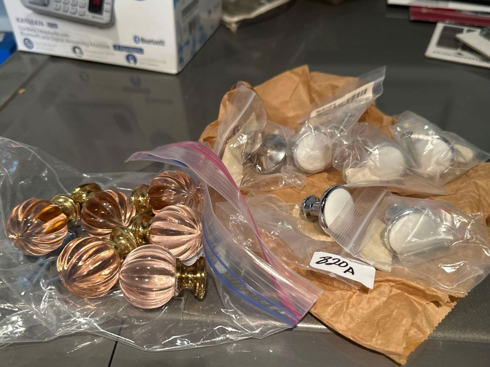 Two Sets Of Six Drawer Pulls, Pink Glass And Brass, Silver And White Ceramic: Two sets of six drawer pulls, pink glass and brass, silver and white ceramic.