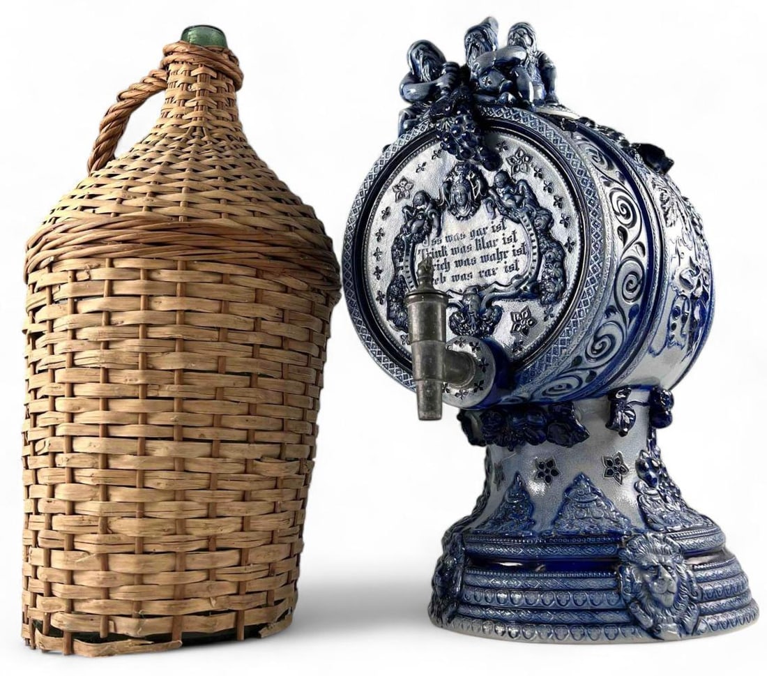 German Cobalt Blue Wine Dispenser & Wicker Wrapped Demijohn Bottle: German Cobalt Blue Wine Dispenser & Wicker Wrapped Demijohn Bottle. Wine dispenser with gnome motif approximately 19.25H x 13.25L x 9.75W in. Demijohn bottle approximately 19.5H x 10.0W in.