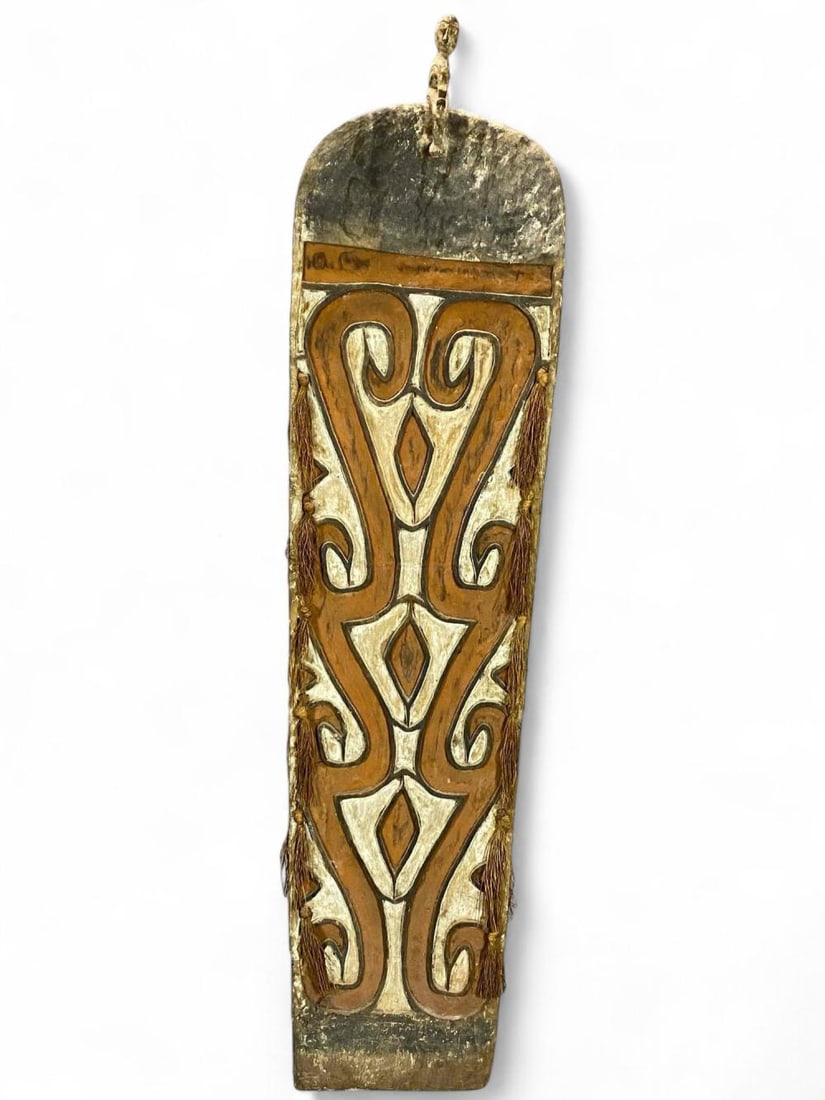Mid 20th Century West Papua Painted Wooden Shield: Mid 20th Century West Papua Painted Wooden Shield. Attached Tag Reads: "ex- George Kennedy UCLA." Approximately 73.625L x 18.375W x 6.0D in.