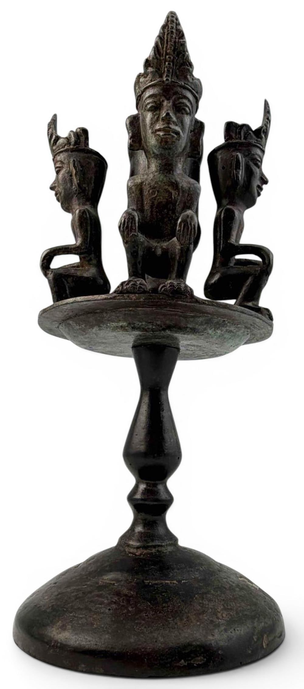 Southeast Asian Figural Bronze Candle Stand: Bronze figural ritual lamp or candle stand, likely Southeast Asian, with a circular dish-form top surrounding a central socket and four seated deity or guardian figures wearing tall headdresses. Appro