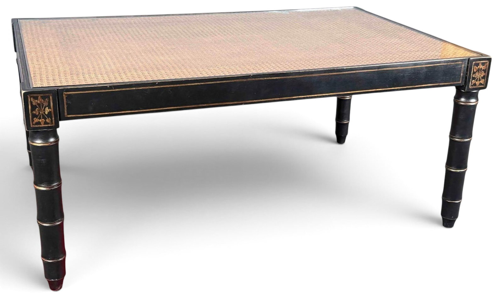 Chinoiserie Cane Top Coffee Table With Gilt Decoration: Rectangular chinoiserie coffee table with woven cane inset top, gilt trim, and gilt floral corner decoration. Raised on turned faux bamboo legs. Approximately 45.87L x 30.0W x 20.12H in.