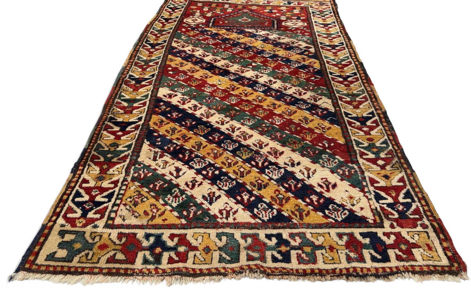 Caucasian Prayer Rug: Hand-knotted wool prayer rug with a pointed mihrab niche above a field of diagonal multicolored bands, each worked with repeating geometric and floral motifs. Framed by multiple borders with stylized 