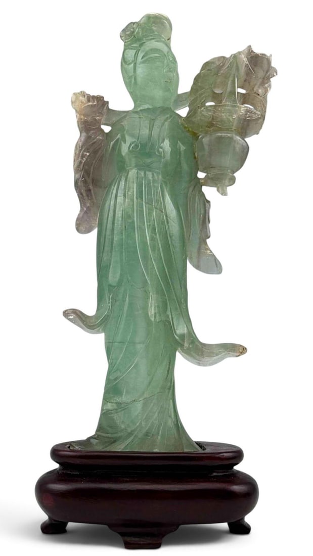 Chinese Carved Fluorite Figure of a Daoist Imortal: Carved pale green & purple fluorite of Daoist immortal, shown standing in flowing robes and holding an openwork floral basket, mounted on a fitted dark wood stand. Approximately 8.25H x 2.25W in.