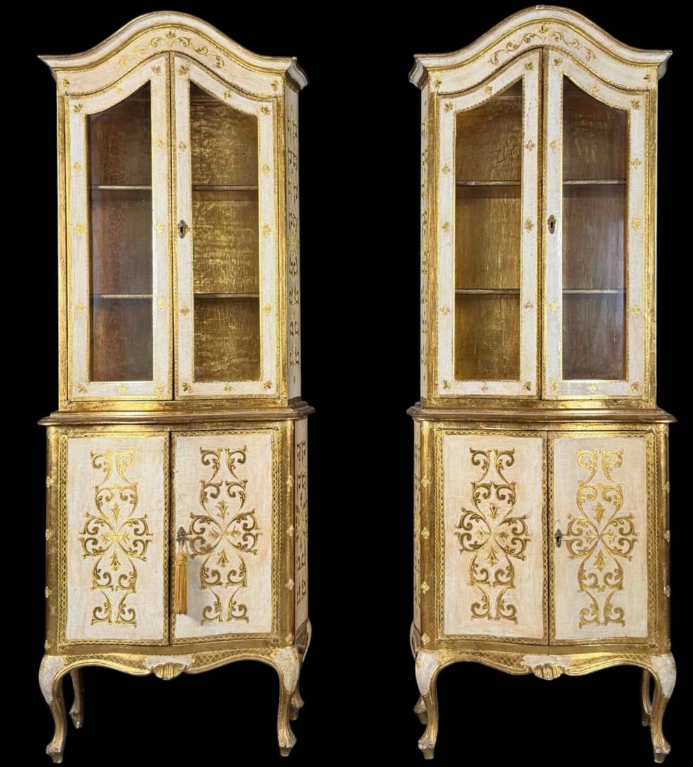 Pair of Italian Venetian-Style Painted and Gilt Display Cabinets, 20th Century: Matched pair of Italian Venetian-style display cabinets featuring cream-painted and parcel-gilt decoration throughout. Each cabinet has a shaped Rococo-style pediment above two glazed doors, opening t