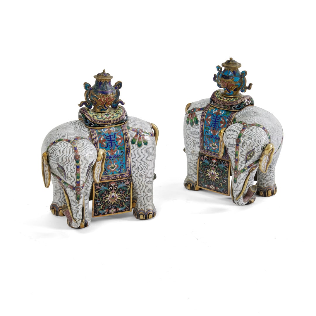 Pair of elephants China, Qing dynasty, late 18th-early 19th Century: Polychrome cloisonné and champlevé enameled metal with extensive gilding, the two animals adorned with floral motifs and the character shou (long life), a vase with a lid and ribbon handles on the b