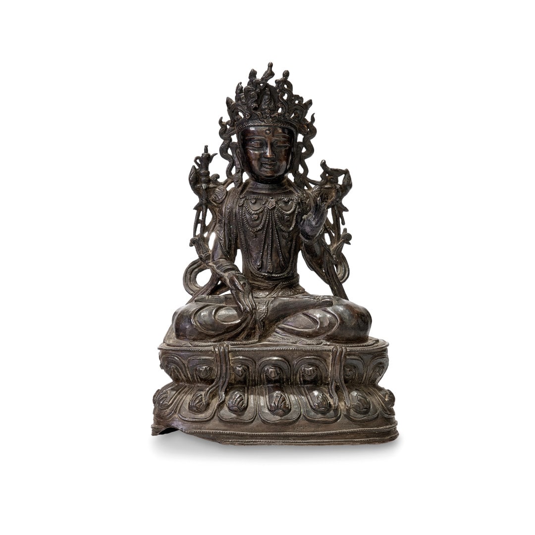 Guanyin China, Ming dynasty, 16th-17th Century: Bronze, the deity seated on a double lotus flower base with legs crossed in lalitasana, dressed in a large robe that leaves the chest exposed with elaborate jewelry, in each hand a flowering stem, nea