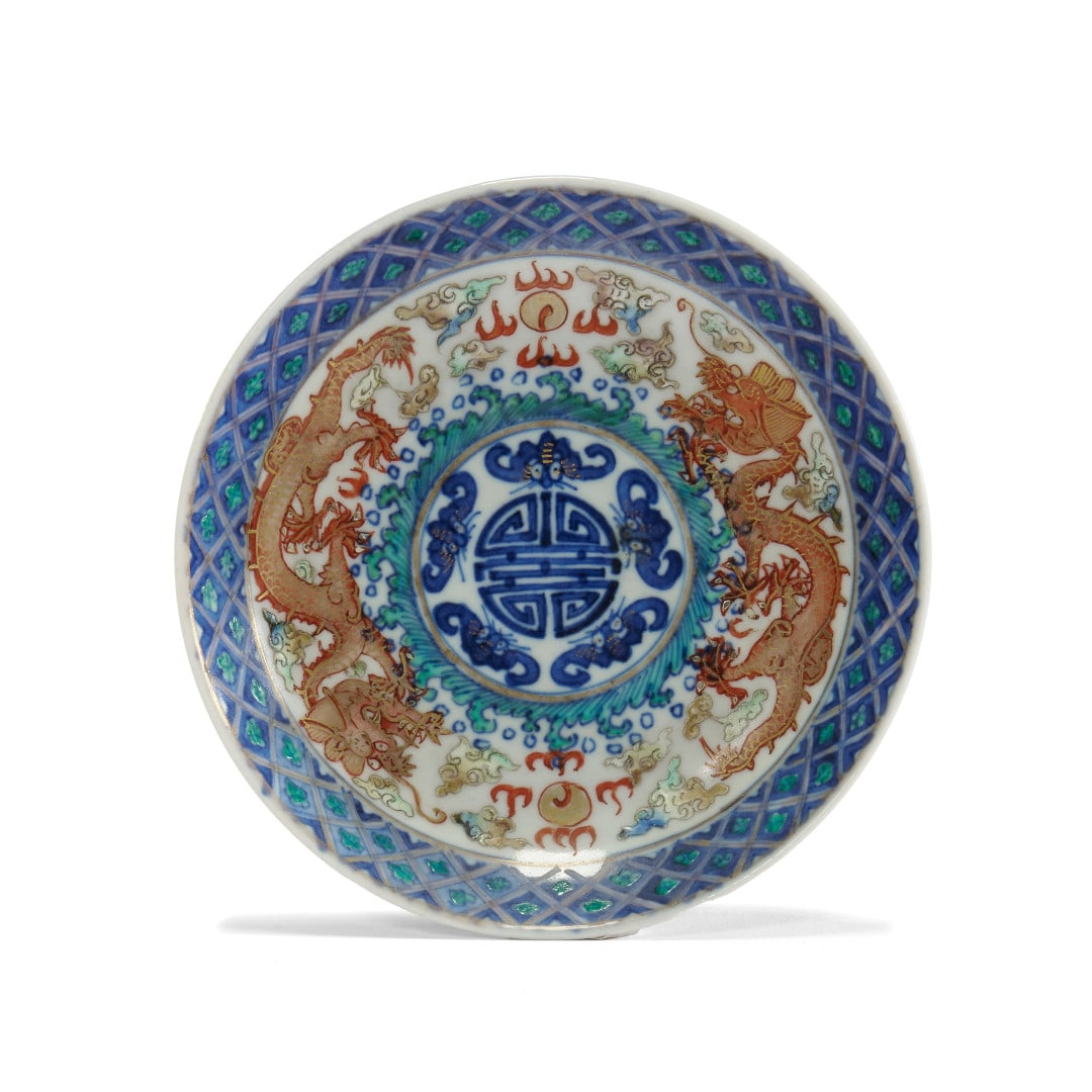 Small dish Cina, 20th century: Porcelain with polychrom enamel and gold decoration, the centre with a medallion with a shou character and bats, enclosed by two dragons flying amidst clouds and darts and a geometric border,