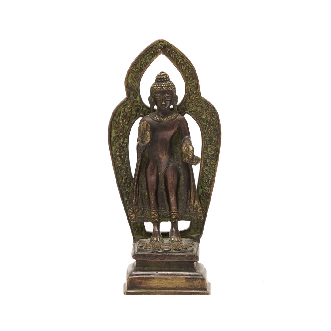 Buddha India, 20th century: Bronze, the deity standing on a rectangular base, his right arm bent at the elbow with his hand open, halo with arabesque decoration in relief. 7.9 x 3.4 x 2 in.