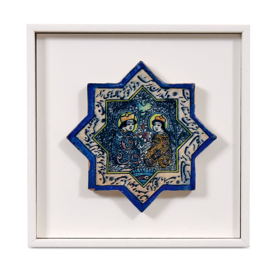 Tile Iran, 19th-20th century: Polychrome enamelled ceramic, modelled with an eight-pointed profile, the centre with a pair of figures with a bird, the composition within a calligraphic border. Measures with frame. 13.6 x 13.6 in.