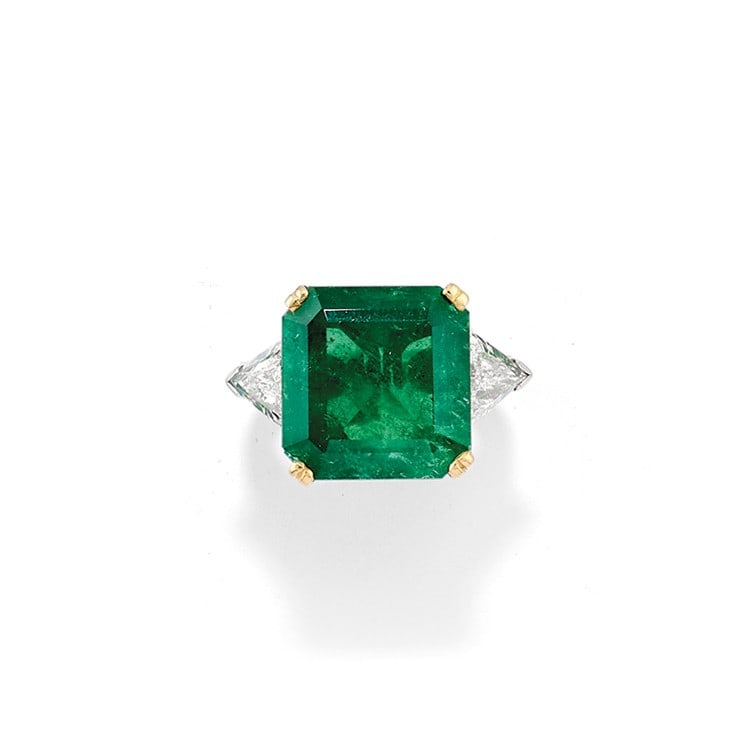 ANELLO IN SMERALDO E DIAMANTI - EMERALD AND DIAMOND: in oro bianco 18 kt con castone a griffe in oro giallo 18 kt che trattiene uno smeraldo naturale taglio quadrato ad angoli tronchi di ct 12,50 ca. affiancato da?due diamanti taglio triangolare di ct 0