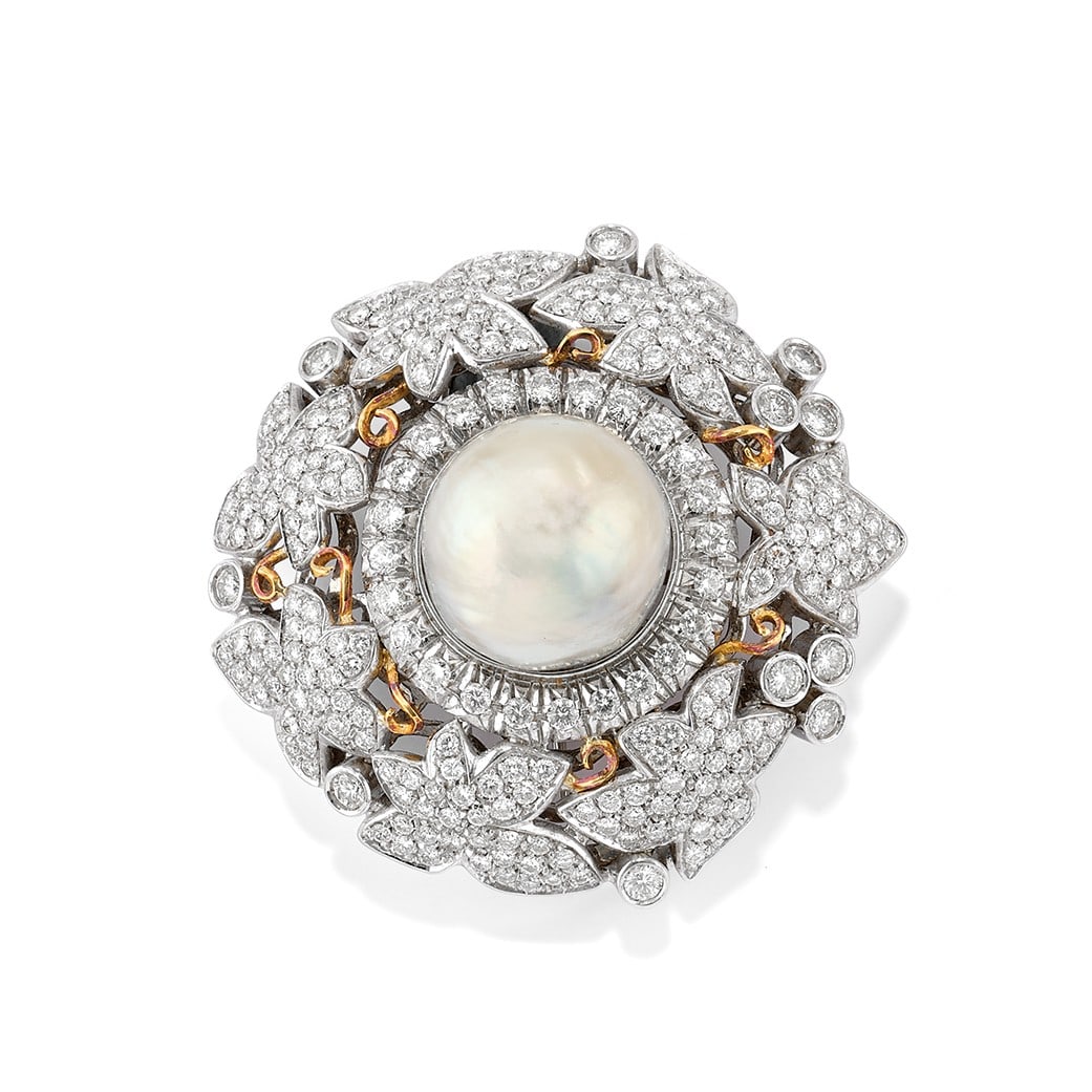 SPILLA IN PERLA COLTIVATA E DIAMANTI - CULTURED PEARL AND DIAMOND BROOCH: in oro bianco 18 kt a forma rotonda con motivo naturalistico in diamanti, con una perla centrale di mm 19,00 ca. contornata da diamanti taglio brillante rotondo di ct 7,50 ca. complessivi. Circa 1970.
